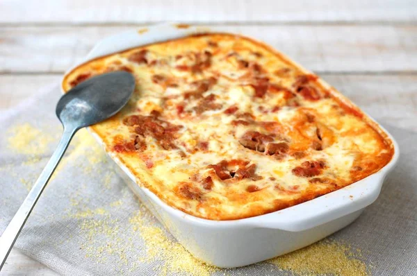 Refeição sem glúten polenta assada com carne de porco, cebolinha, especiarias em panela branca sobre pano cinza sobre fundo branco de madeira — Fotografia de Stock