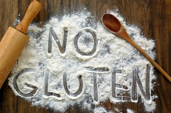 Gluten free flour with text no gluten in English language with wooden spoon and rolling pin on dark brown wooden background