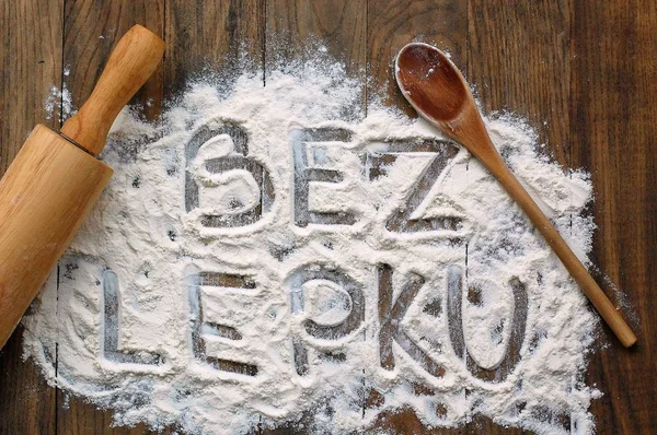 Gluten free flour with text gluten free in Czech language with wooden spoon and rolling pin on dark brown wooden background
