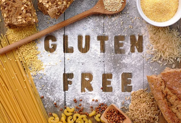 Gluten free flour and cereals millet, quinoa, corn flour polenta, brown buckwheat, basmati rice and pasta with text gluten free in English language with wooden spoon on brown wooden background