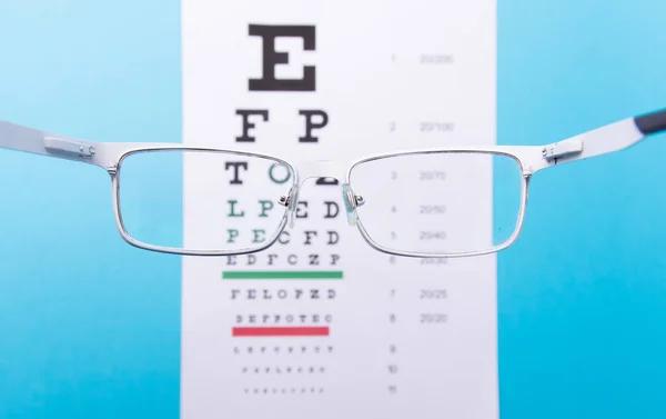 Hand-held glasses, view of the Snellen chart. Blue background — Stock Photo, Image