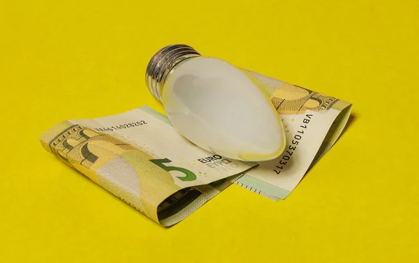 Den elektriska glödlampan och eurosedlar på en gul bakgrunds — Stockfoto