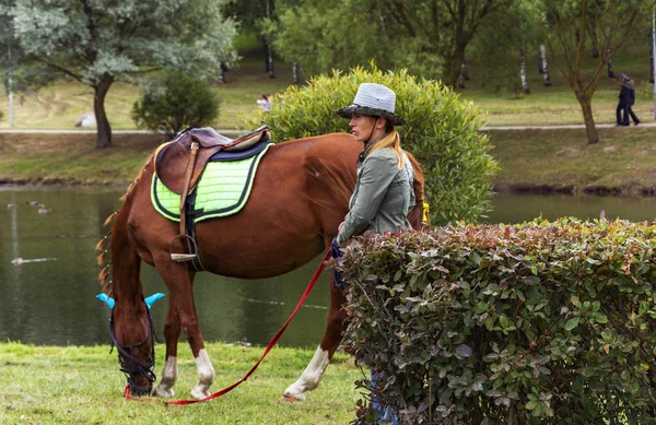 Chica en un sombrero de vaquero y caballo mordisqueando hierba — Foto de Stock