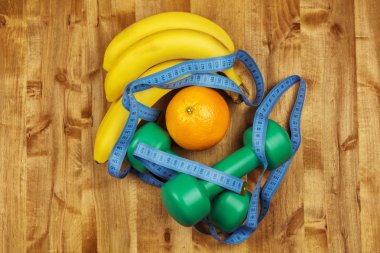 İki dambıl, bir santimetre, muz ve portakal bir tahtaya yalan