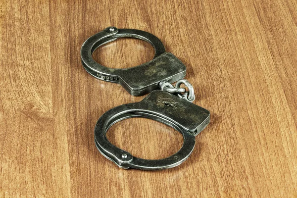 На деревянном столе лежат металлические наручники — стоковое фото