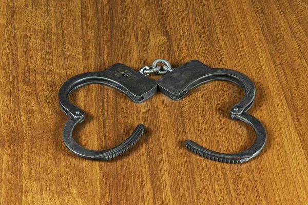 На деревянной поверхности металлические наручники — стоковое фото