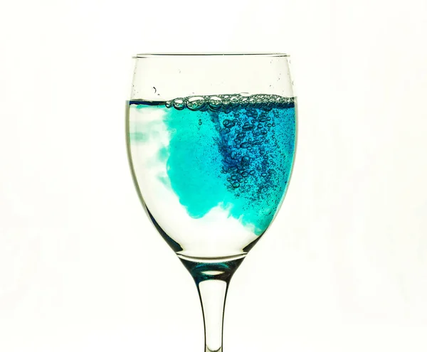 Um copo de vidro com água clara é preenchido com um líquido azul — Fotografia de Stock