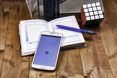 Ahşap yüzeyde olan kitap, bir defter bir kalem, Rubik küp ve bir akıllı telefon ile