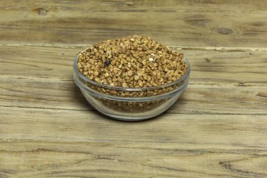 Bir cam vazo karabuğday kabuğu çıkarılmış tane ile ahşap bir yüzey üzerinde duruyor