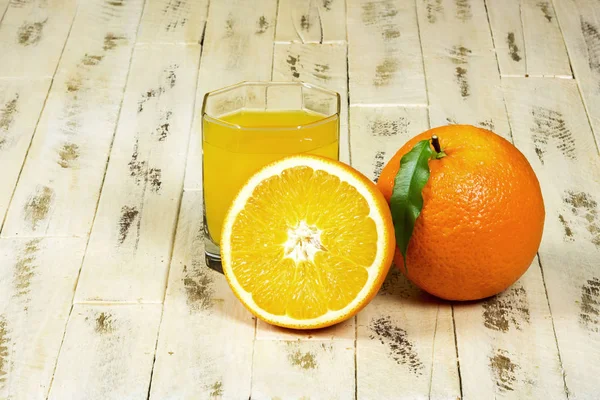 Orangen und ein Glas Orangensaft auf Holzoberfläche — Stockfoto