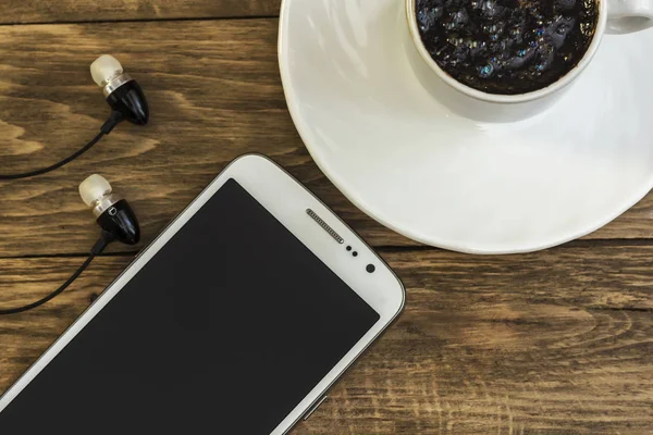Tasse à café sur soucoupe, smartphone et écouteurs sur surface en bois — Photo