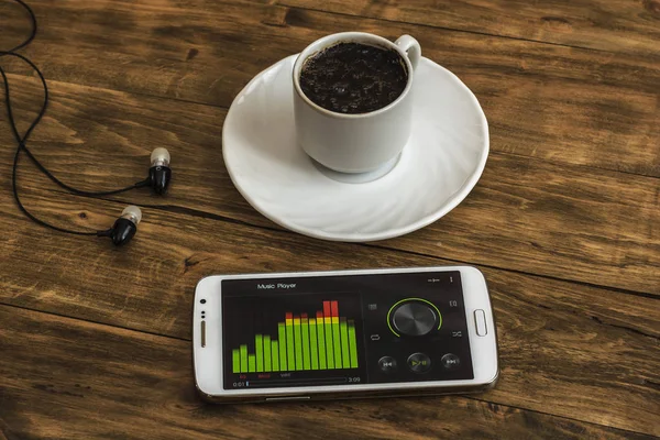 Tasse de café sur soucoupe, écouteurs et smartphone avec égaliseur sur — Photo