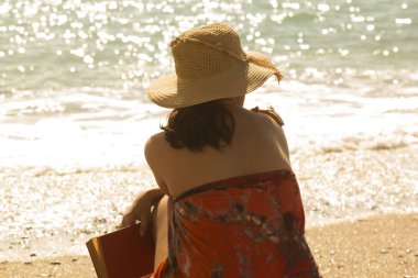 Güzel bir kadın sahilde okuyor.