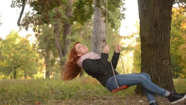 Red-haired woman riding on a swing in the park — Stock Video