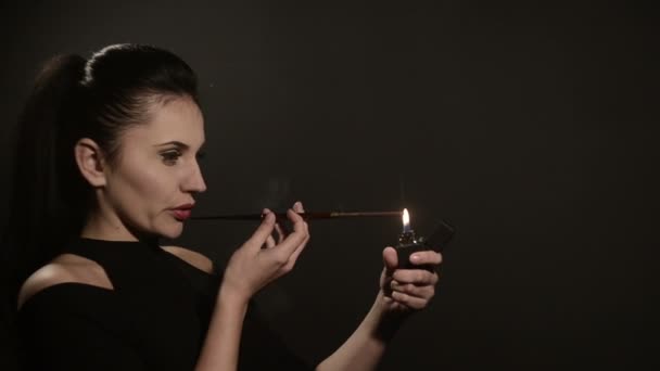 Beautiful woman lights a cigarette in a mouthpiece on a black background — Stock Video