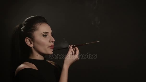 Beautiful woman smokes a cigarette in a mouthpiece on a black background — Stock Video