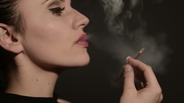 Hermosa mujer fuma un cigarrillo sobre un fondo negro — Vídeos de Stock