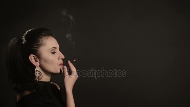 Belle femme fume une cigarette sur un fond noir — Video