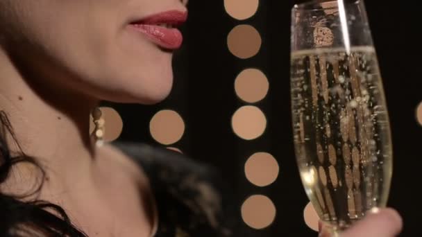 Женщина пьет шампанское из бокала на фоне праздничных огней ночью — стоковое видео