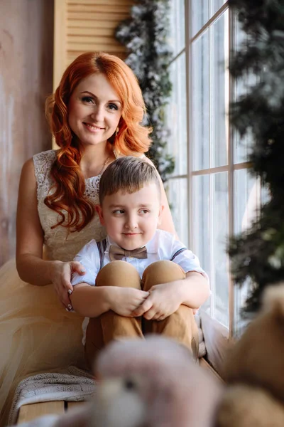 Mutter und Sohn sitzen am Fenster im Raum mit der Weihnachtsdekoration. — Stockfoto