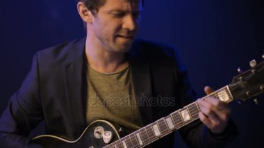 Bir adam bir elektro gitar çalar ve karanlık bir odada şarkı söylüyor