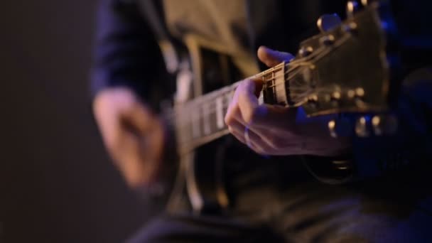 Hombre está sentado y tocando la guitarra en una habitación oscura — Vídeo de stock