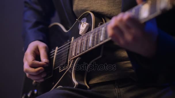 Hombre está sentado y tocando la guitarra en una habitación oscura — Vídeo de stock