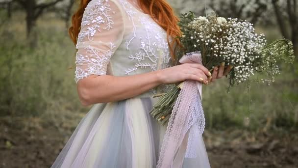 Mulher bonita de cabelos vermelhos em um vestido luxuoso está segurando um buquê de primavera no jardim florido — Vídeo de Stock