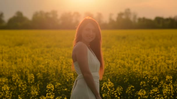 Молодая рыжая женщина с летящими волосами посреди цветущего поля — стоковое видео