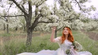 Kızıl saçlı kadın bir elbise giymiş bir çiçek bahçesinde çimenlerin üzerinde oturur