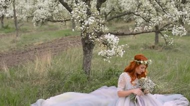 Kızıl saçlı kadın bir elbise giymiş bir çiçek bahçesinde çimenlerin üzerinde oturur