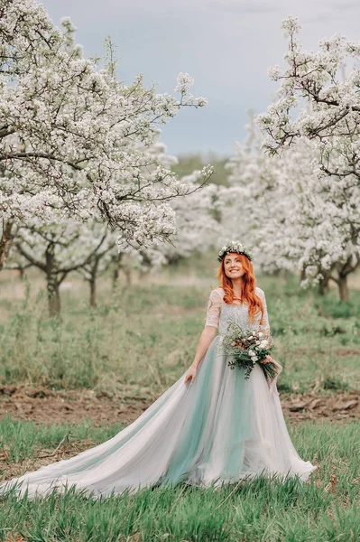 Jeune femme dans une robe de luxe est debout et souriant dans un jardin fleuri — Photo