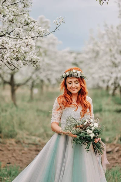 Young woman in a luxurious dress is standing and smiling in a blooming garden — Stock Photo, Image