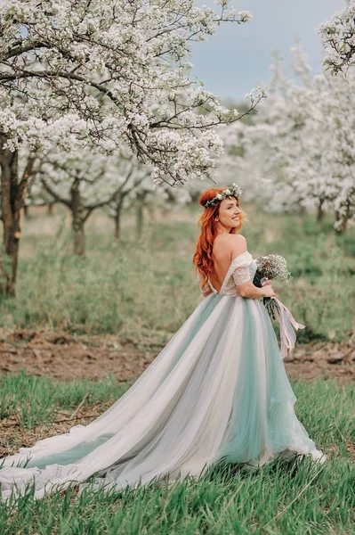 Junge Frau in luxuriösem Kleid steht in einem blühenden Garten — Stockfoto