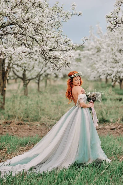 Jeune femme dans une robe de luxe est debout dans un jardin en fleurs — Photo