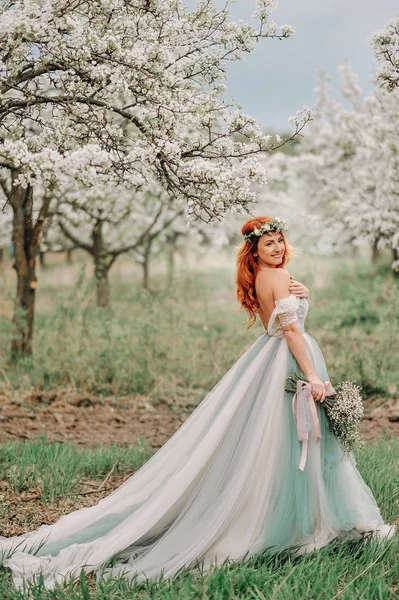 Jeune femme dans une robe de luxe est debout dans un jardin en fleurs — Photo