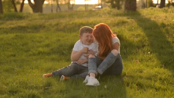Мать и сын веселятся на улице, сидя на траве — стоковое видео
