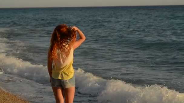 Молодая женщина с летящими волосами стоит на скалистом пляже Адриатического моря — стоковое видео