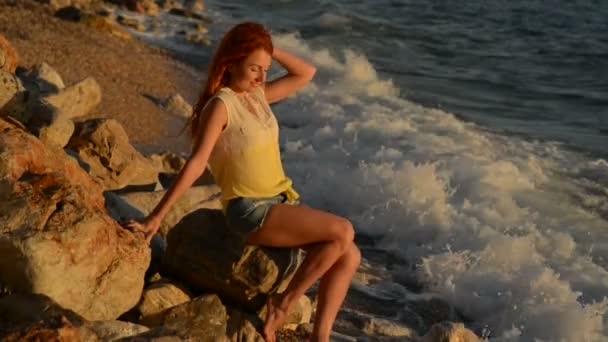 Ung kvinna med flygande hår som sitter på den steniga stranden av Adriatiska havet — Stockvideo