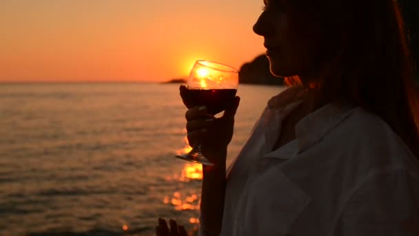 Genç kadın içecekler kırmızı şarap cam, deniz kıyısında günbatımı — Stok video