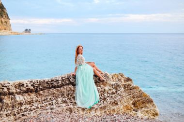 Adriyatik Denizi kıyısında büyük bir taş üzerinde bir nane içinde genç bir kadın oturur