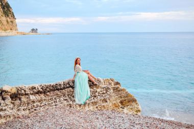Adriyatik Denizi kıyısında büyük bir taş üzerinde bir nane içinde genç bir kadın oturur