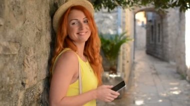 Kızıl saçlı kadın turist bir smartphone bir antik kent sokakta kullanır.