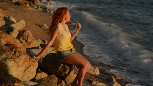 Молода жінка з польотом волосся сидить на кам'янистого пляжу Адріатичного моря — стокове відео