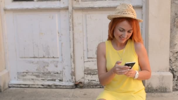 Turista mujer pelirroja utiliza un teléfono inteligente en la calle de una antigua ciudad — Vídeo de stock