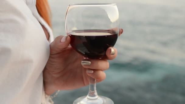 Copa de vino tinto en las manos de una mujer contra el mar — Vídeo de stock