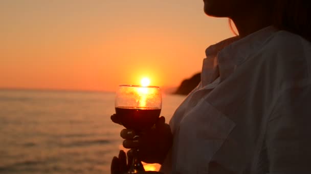 Νεαρή γυναίκα με ένα ποτήρι κόκκινο κρασί, ηλιοβασίλεμα δίπλα στη θάλασσα — Αρχείο Βίντεο
