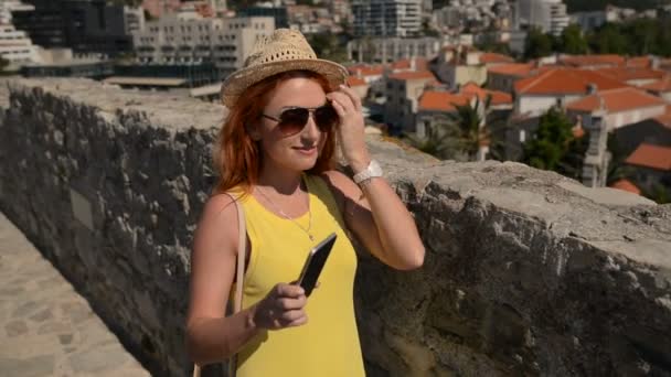 Jonge vrouw in bril en een hoed maakt selfie op de achtergrond van een oude stad — Stockvideo