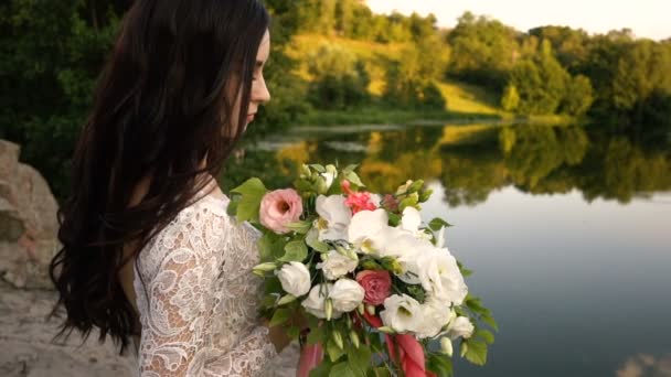 Giovane sposa tenendo bouquet sulla riva del fiume, primo piano — Video Stock