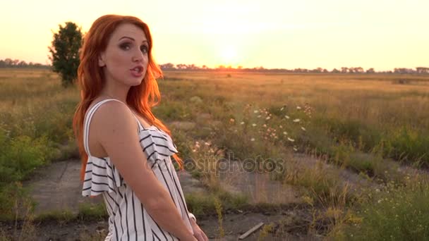 Red-haired woman looking at the camera and smiling at sunset — Stock Video